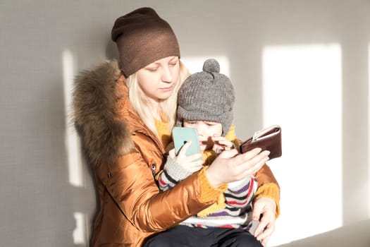 A mother with a small child in her arms is warmly dressed in outerwear, counting money in her purse. The concept of the economic crisis and large utility bills in homes