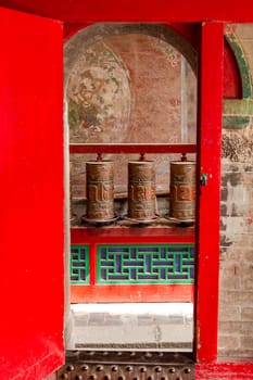 Prayer wheels behind a gate in a Tibetan temple of the Kumbum Jampaling monastery complex in Xining, China, Asia