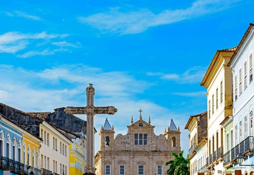 Large crucifix in the central square of the historic district of Pelourinho in the city of Salvador in Bahia with baroque church and colonial houses in the background