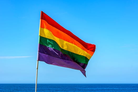 Lbgtq+ flag in the blue sky of the city of Rio de Janeiro, Brazil with sea in background