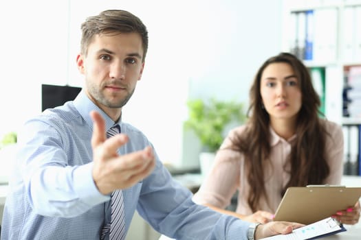 Businessman with woman stretches his hands forward sitting in office. Business consultant concept