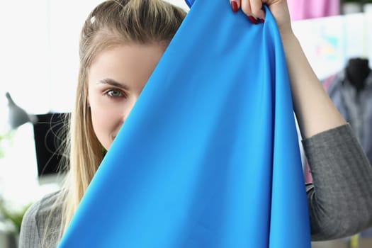 Portrait of beautiful seamstress woman holding blue fabric. Fashion tailoring training in design studio