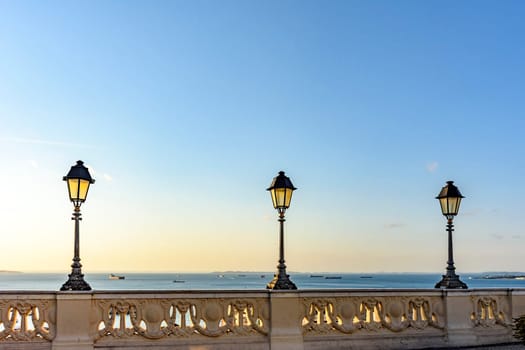 Old colonial style lanterns lighting on walls in the streets of Salvador with the All Saints bay in the background with their boats during the sunset