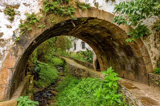 Old historic stone tunnel passing through vegetation and old colonial-style houses in the historic city of Ouro Preto in the state of Minas Gerais.