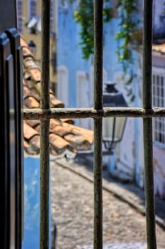 Old street with cobblestone pavement in the Pelourinho neighborhood of Salvador, Bahia seen through the window and bars of a historic church