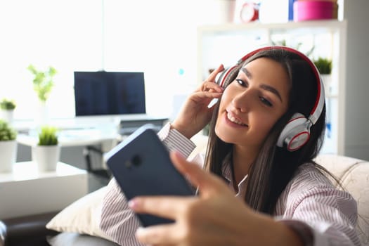 Beautiful woman in headphones holding smartphone at home. Applications for listening to quality music on your phone