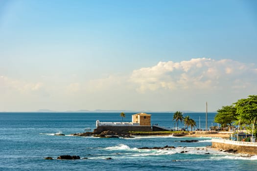 Scenic view of the old colonial Portuguese Fort Santa Maria in Barra beach, Salvador, Brazil with palm trees standing above the rugged shoreline