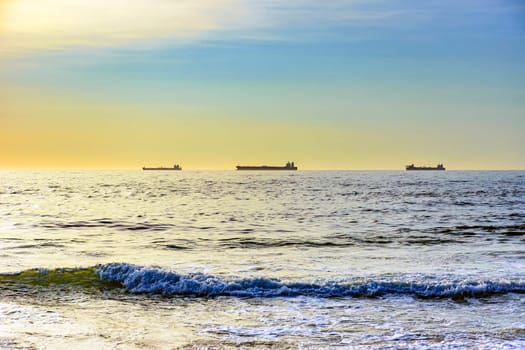 Ships moored on the horizon waiting to go to port during dawn on Ipanema beach in Rio de Janeiro