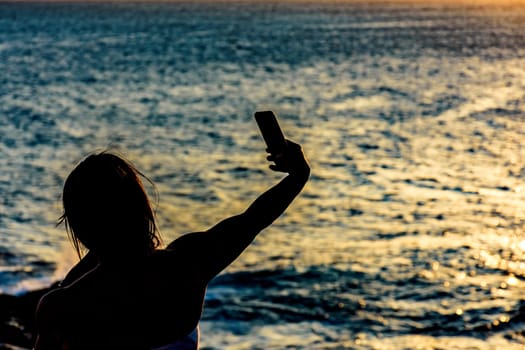 Silhouette of girl with smartphone taking selfie in the summer during the sunset in Salvador city, Bahia