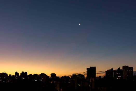 Skyline of Porto Alegre city at dusk with the moon in the sky with buildings silhuette