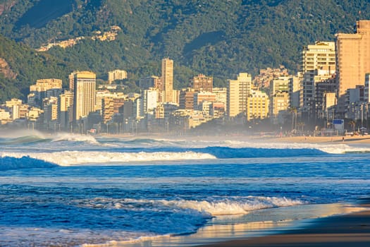 Sunrise on Ipanema beach in Rio de Janeiro with the sea, forest, waves and city buildings