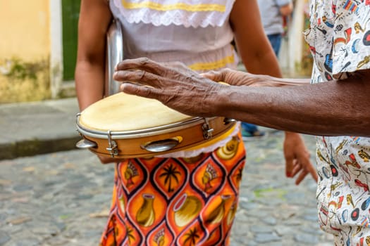 Tambourine player with a woman in typical clothes dancing in the background in the streets of the Pelourinho district in Salvador, Bahia