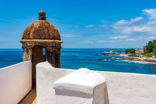 Wall and guardhouse of an old historic fort on the edge of the city of Salvador in Bahia with the sea and the city in the background
