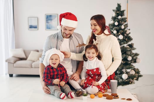 Sits against fir. Beautiful family celebrates New year and christmas indoors at home.