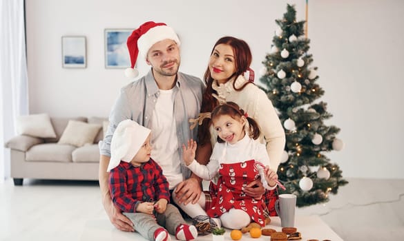 Sits against fir. Beautiful family celebrates New year and christmas indoors at home.