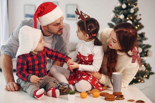 Sits against fir. Beautiful family celebrates New year and christmas indoors at home.