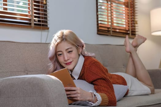 Attractive young Asian woman sits in the minimal and comfortable living room enjoying reading a book...
