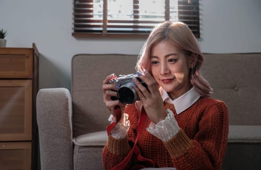 Young beautiful Asian woman relaxing in living room at home, reading books, drinking coffee and using phone in the morning with happy feeling..