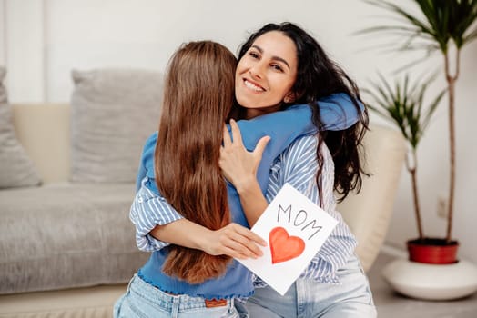 Happy mother's day. Child daughter congratulates mom and gives her flowers tulips and postcard. Mum and girl smiling and hugging. Family holiday and togetherness. Arab mom is happy to return to the home atmosphere and receive an unexpected gift from her daughter.