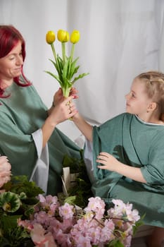 Amazing pretty mother and daughter having fun with flowers in 8 March or in Mother's day. Red haired mom and small little blonde girl having lovely free time on white background in studio