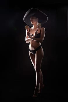 Silhouette of a beautiful young girl in black underwear and Mexican hat on a dark background. Exotic model posing naked in the studio. Body portrait of sexy girl