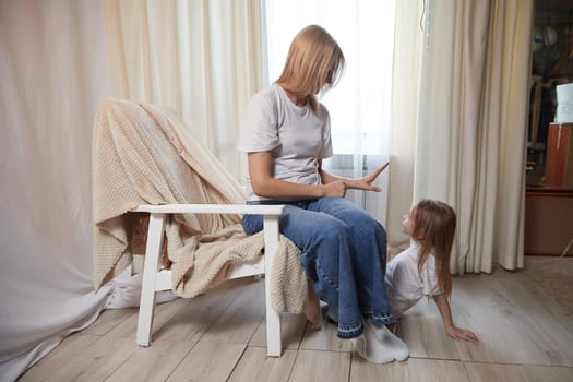 Happy loving family with mother and daughter in living room. Woman mom and small child girl playing and having convercation inside of home