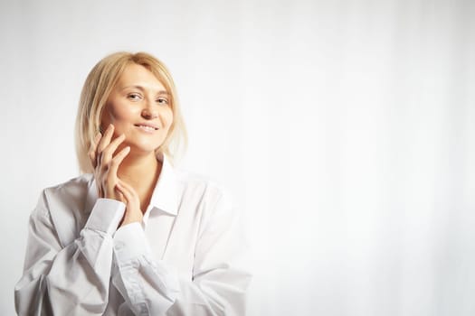 Portrait of a pretty blonde smiling woman posing on white background. Happy girl model in white shirt posing in studio. Copy space