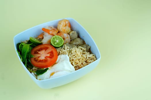 Soup noodle with shrimps, meat balls, eggs and vegetables served in white bowl.