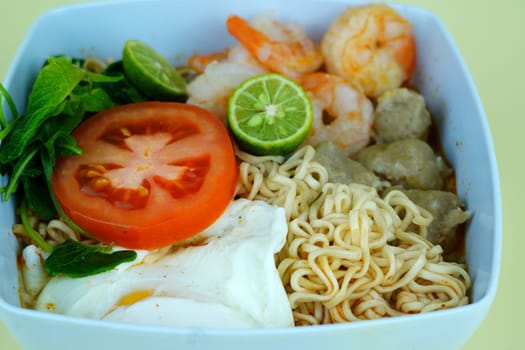 Soup noodle with shrimps, meat balls, eggs and vegetables served in white bowl.