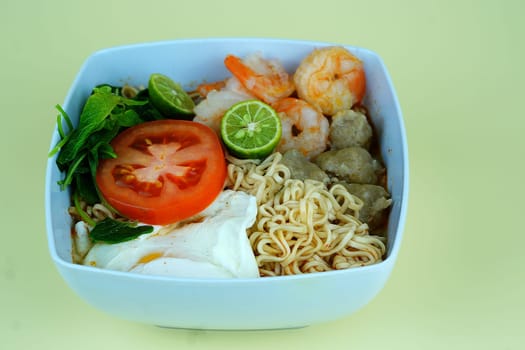 Soup noodle with shrimps, meat balls, eggs and vegetables served in white bowl.