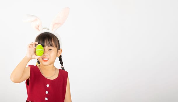 Happy Easter Day. Smile Asian little girl wearing easter bunny ears holding colorfull eggs closes eyes with testicles isolated on white background with copy space, Happy child in holiday