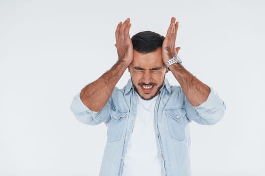 Feels headache. Young handsome man standing indoors against white background.