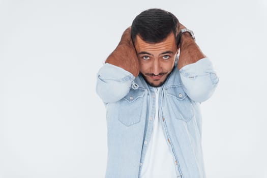 Stressful young man standing indoors against white background.