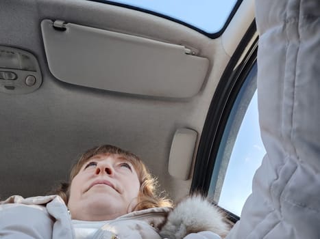 Woman sitting in the car in road trip. Blonde senior Woman driving transport. Lady travelling in cold time