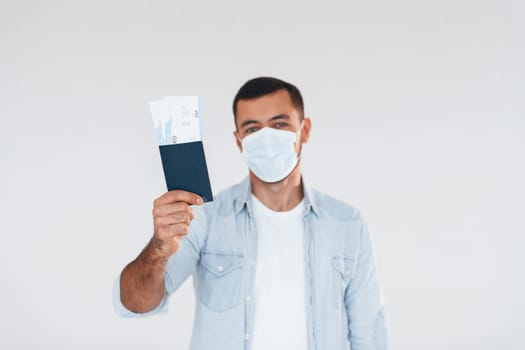 Tourist with ticket. Young handsome man standing indoors against white background.