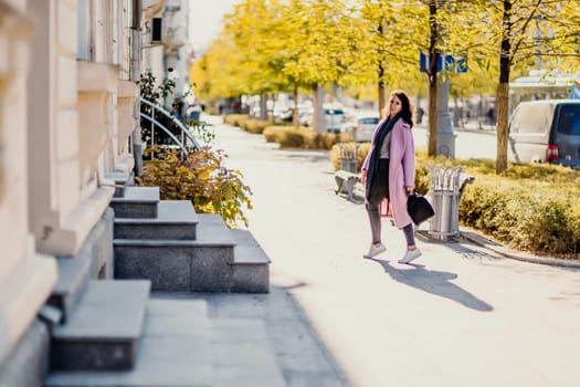 Woman autumn city. A woman in a pink faux fur coat posing on a city street in autumn on a sunny day. Trees with yellow foliage along the street