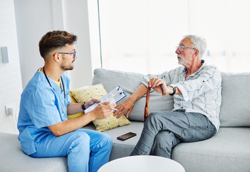 Doctor or male caregiver with senior man holding a cane on sofa at home or nursing home