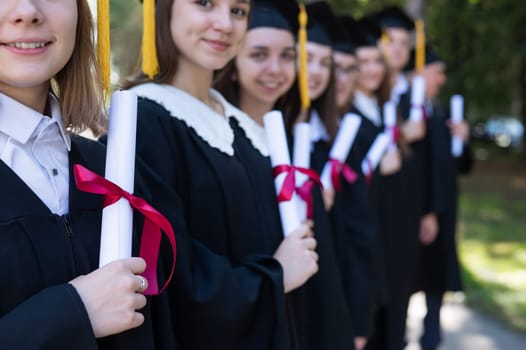 Row of young people in graduation gowns outdoors. Age student