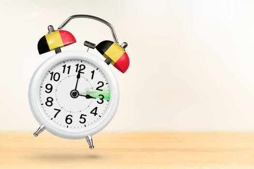 Time change in Belgium, spring forward. Summer time concept, over white background. A white alarm clock with a minute hand indicates that the time has been moved forward an hour with copy space