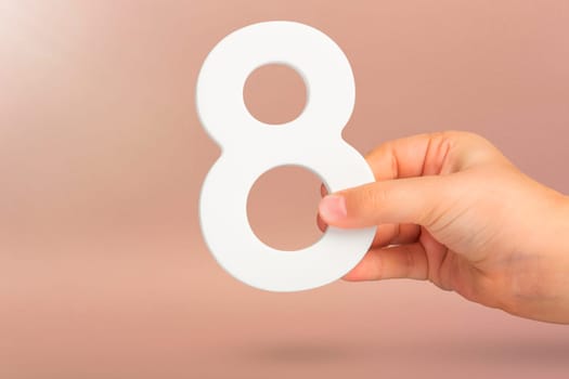 Eight in hand. A hand holds a white number 8 on a red background. Concept with number eight. Birthday 8 years, percentage, eighth grade or day, international women's day