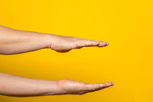 Strong hands of man in parallel offering something imaginary inside, advertising concept with copy space. Isolated on yellow background