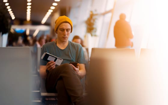 A young man sits at the airport and checks in for the next flight via an app on his phone, waits for the plane and works while traveling.