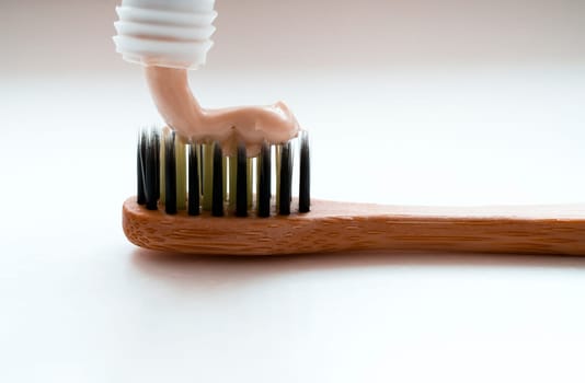 Stylish bamboo toothbrush on a light background in the bathroom with a toothpaste from a tube, close-up macro view.