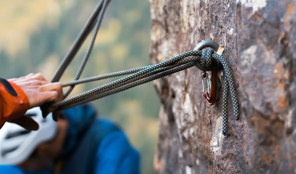 Climbing station on bolts on a rock, people are learning mountaineering in a camp outdoor, a woman's hand checks the reliability of belay, rope, carabiners.