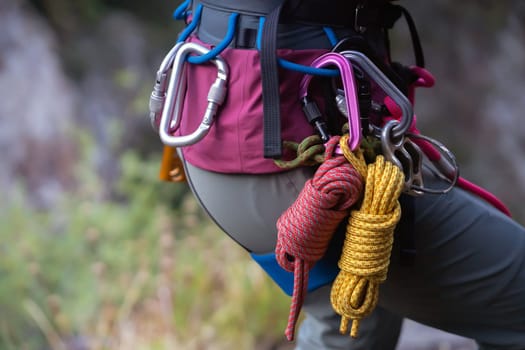 Climbing equipment, ropes, carabiners, harness, belay, close-up of a rock-climber put on by a girl, the traveler leads an active lifestyle and is engaged in mountaineering.