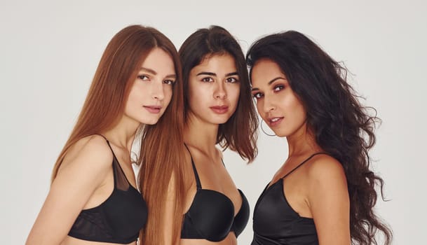 In black bra. Three young women in lingerie together indoors. White background.