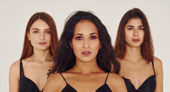 In black bra. Three young women in lingerie together indoors. White background.