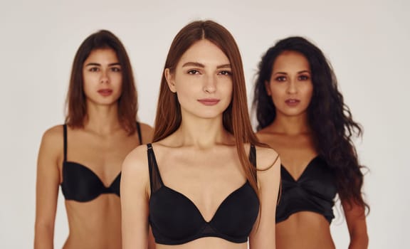 In black bra. Three young women in lingerie together indoors. White background.