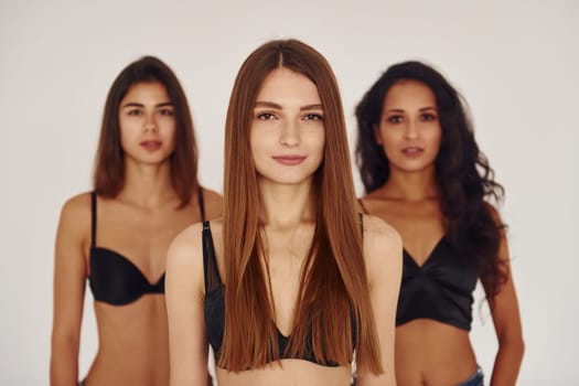 In black bra. Three young women in lingerie together indoors. White background.