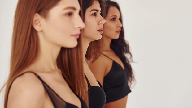 Side view. Three young women in lingerie together indoors. White background.